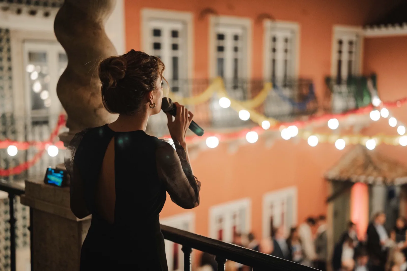A singer performing from a balcony at a Lisbon street party, lights strung across the façade.